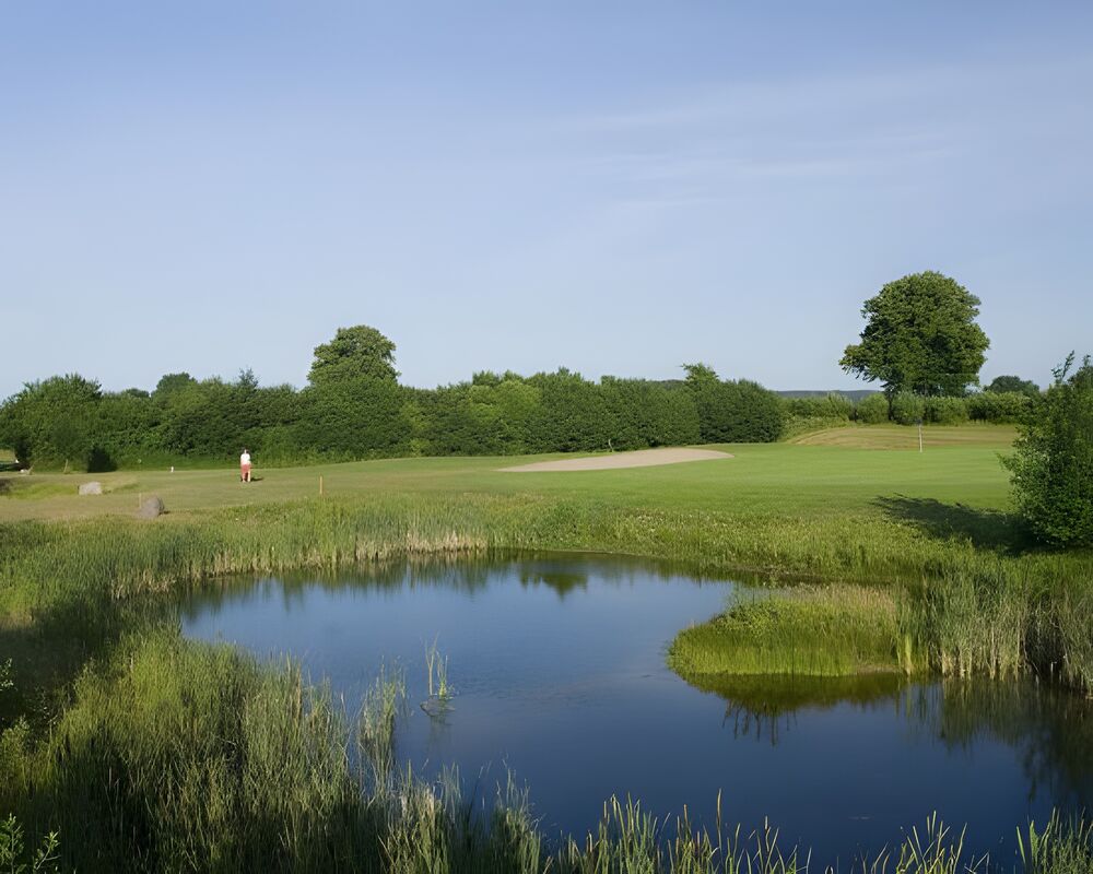 Golfplatz mit großem Teich und einem Golfer im Hintergrund.