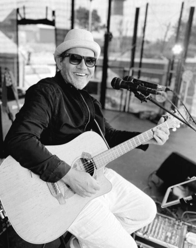 Sänger mit Gitarre und Hut sitz auf einer großen Live- Bühne.