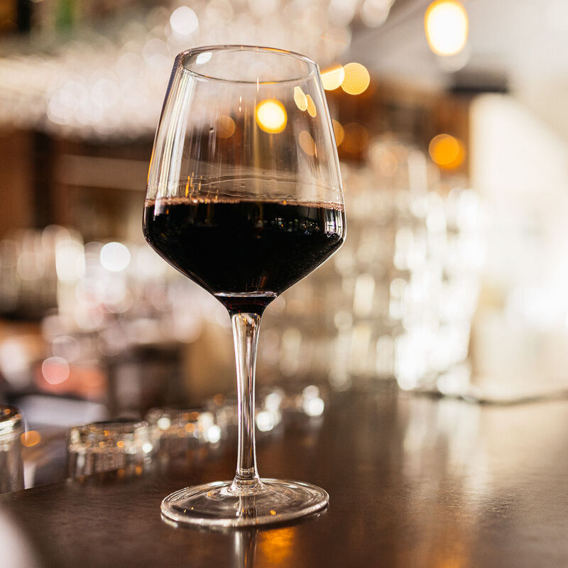 Ein Rotweinglas steht auf einer edlen hölzernen Bartheke mit sonnigen Lichtreflexen.